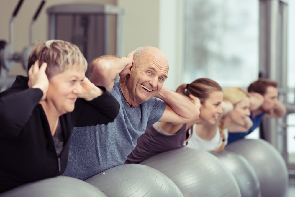 https://f.hubspotusercontent30.net/hubfs/14500231/Elderly%20couple%20doing%20pilates%20class%20at%20the%20gym%20with%20a%20group%20of%20diverse%20younger%20people%20balancing%20on%20the%20gym%20ball%20with%20raised%20arms%20to%20tone%20their%20muscles%20in%20an%20active%20retirement%20concept.jpeg